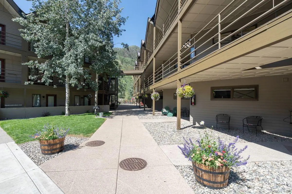 An inviting courtyard area with flower pots, shaded walkways, mature trees, and architectural details of the building. Residents are pictured enjoying the outdoors, socializing, and appreciating the serene gardens.