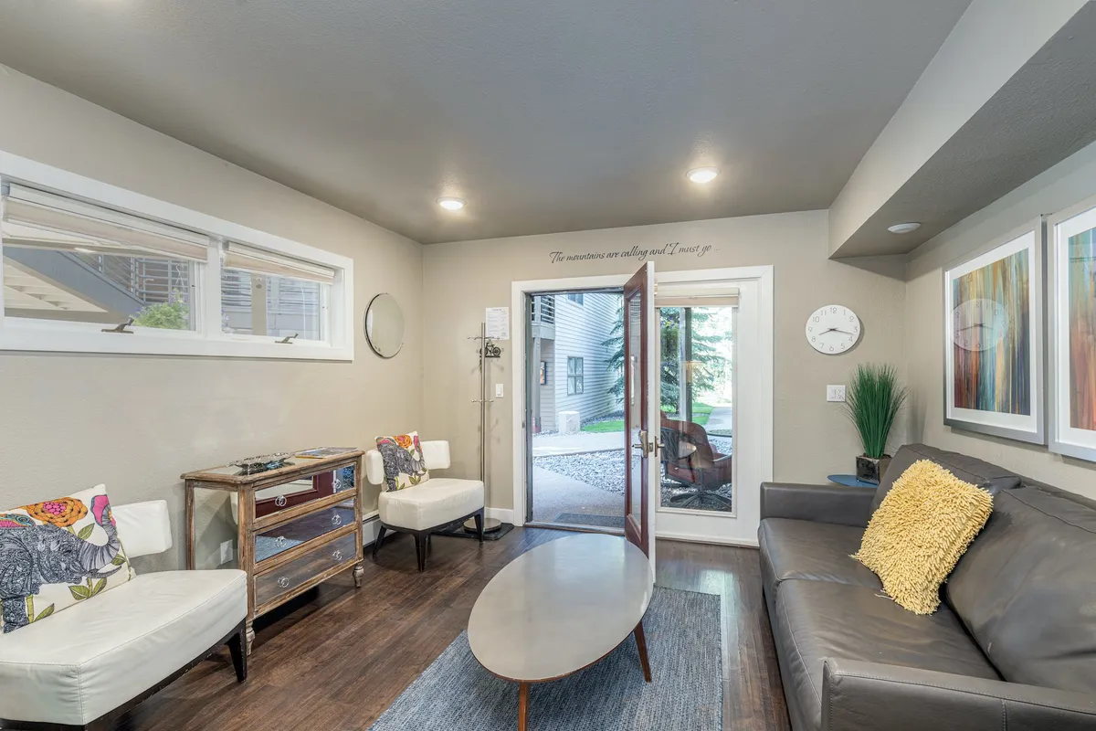 An open-concept living area featuring a cozy sofa with decorative pillows, a coffee table, artwork, and an open door that brings in natural light. The room is designed for both relaxation and conversation, capturing the essence of a welcoming gathering space.